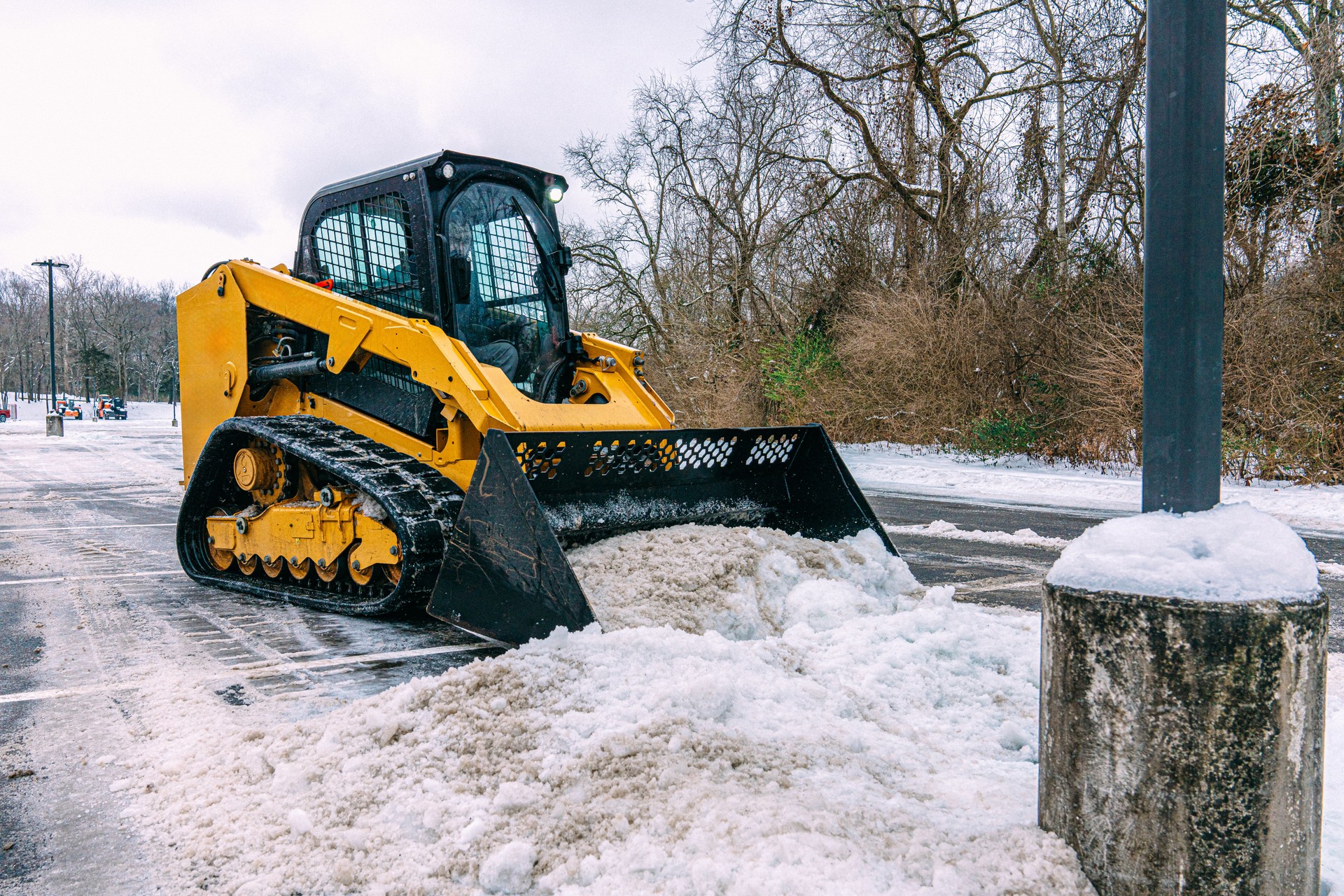 Snow Removal Company Man operating a Bulldozer to remove snow and ice from a parking lot in Winter